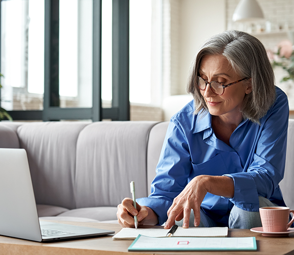 Senior woman with glasses filling out forms on coffee table