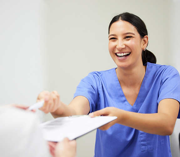 Dental team member in blue shirt handing clipboard to patient