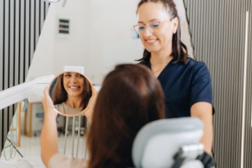 Dentist watching as patient checks her smile in the mirror