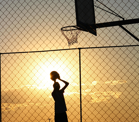 Man about to shoot basketball while sun is setting