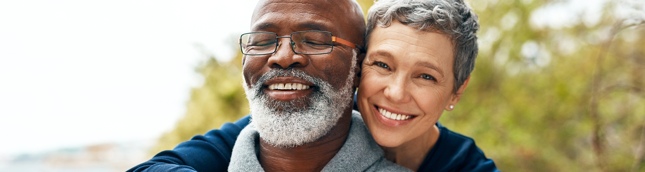 Senior woman hugging senior man with glasses from behind